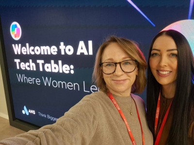 Two women smiling in front of a large digital screen